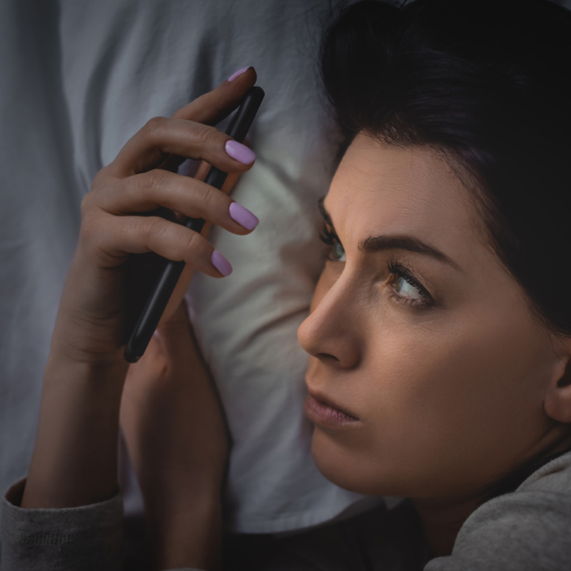 woman-with-insomnia-staring-at-smartphone-on-bed-sleep-wake-disorders